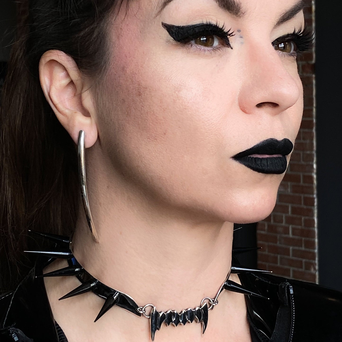 Long minimalist sterling silver curved spike earrings on a dominatrix.
