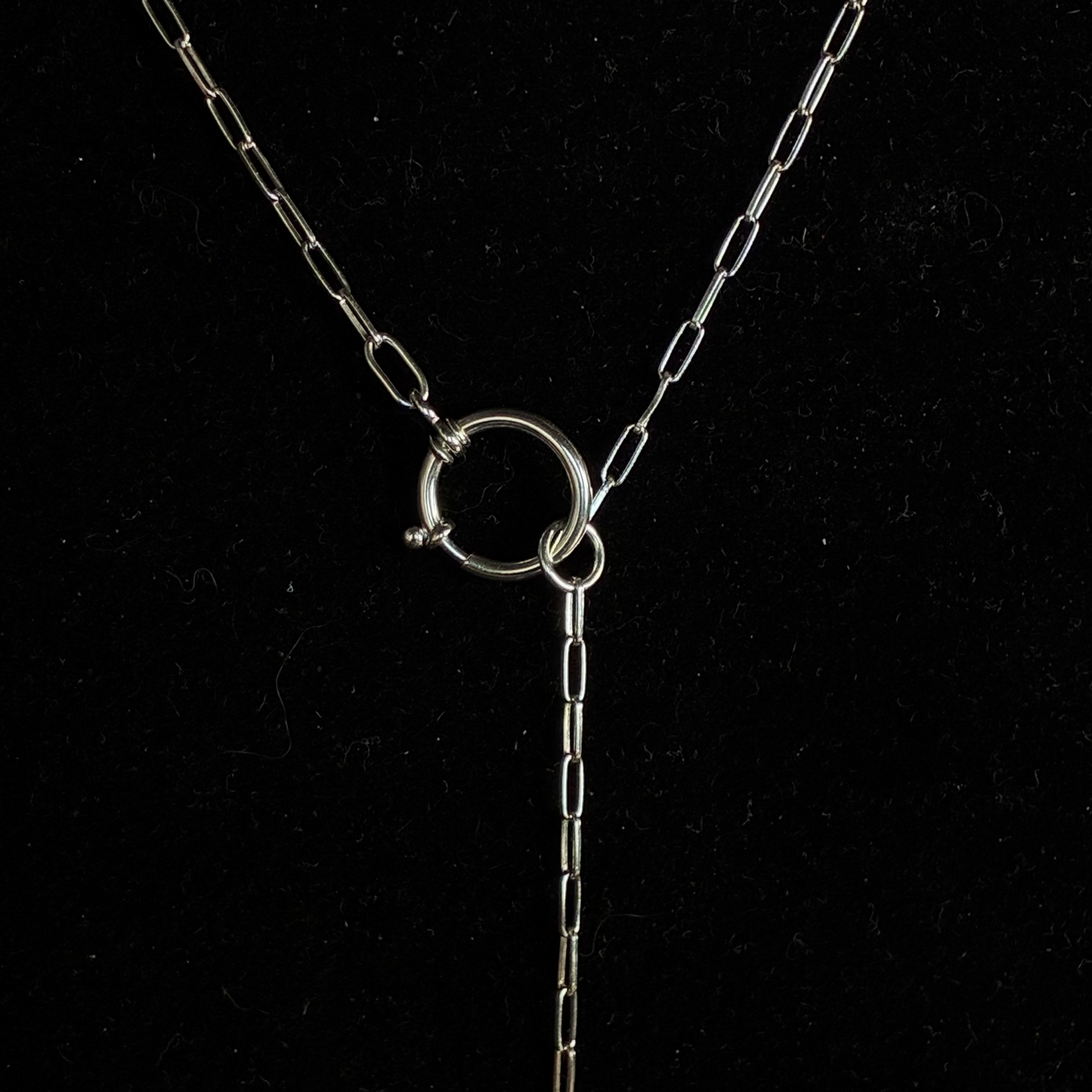 A silver chain necklace with a circular ring clasp and a long drop chain, displayed on a black background.